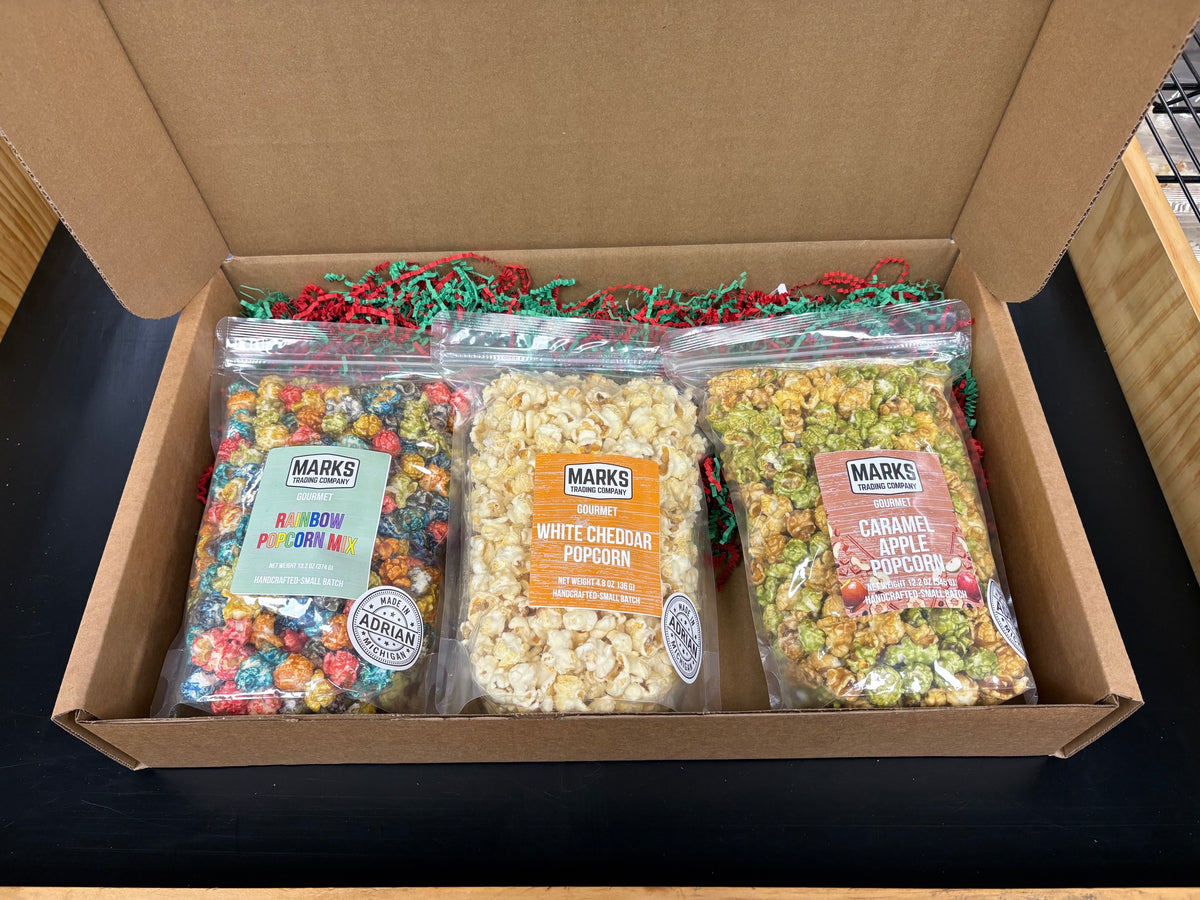 Marks Trading Company gourmet popcorn subscription box featuring three bags of rainbow, white cheddar, and apple flavors